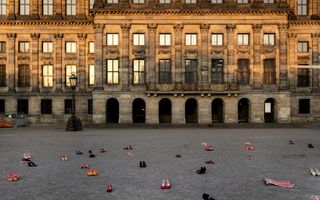 Rode schoenen staan verspreid over De Dam. Op de achtergrond Het Paleis op De Dam. 