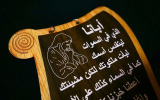 Een houten bord met daarop Arabische letters en een afbeelding van iemand die bidt.