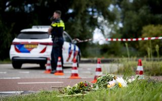 Bloemen in het gras, op de achtergrond een politieafzetting met daarbij een agent en een politieauto