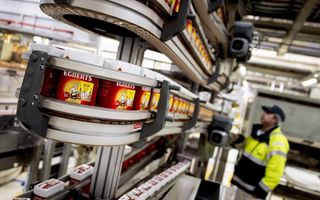 Werknemer Douwe Egberts in gele jas staat bij machine voor verpakken koffie van Douwe Egberts