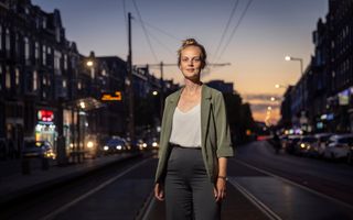 Een jonge vrouw staat in de schemer met achter haar een vrij drukke straat.