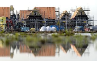 Nieuwe huizen in aanbouw. Ze staan in de stijgers. Op de voorgrond een waterplas, waarin de huizen weerspiegelen.
