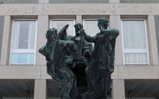 Een bronzen beeld voor een betonnen gebouw, waarop de woorden Paleis van Justitie staan.