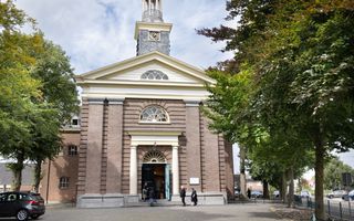 Oud kerkgebouw, met een toren. Bezoekers lopen naar binnen.