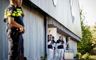 Jongeren met zwarte T-shirts met de tekst ”Meat the victims” staan bij een stal. Op de voorgrond kijken twee politieagenten toe.