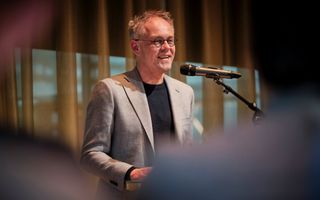 Kees van Ekris, een man met grijs haar, grijs colbert, achter de microfoon.