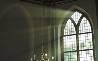 Zonnestralen breken door een glas-in-loodraam in een oude kerk.