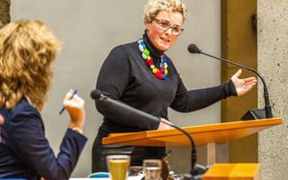 Vrouw staat met expressief gebaar achter het spreekgestoelte van de Tweede Kamer.