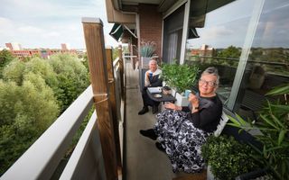 Twee oudere vrouwen met grijs haar drinken een kopje koffie op een balkon.