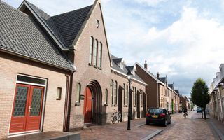 Bakstenen kerkgebouw met rode deur tussen huizen.