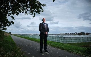 Dominee Tekelenburg, een man in pak, bril op, en op de achtergrond glazen kassen.