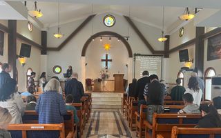 Kerkzaal met mensen op banken; sommigen staan.