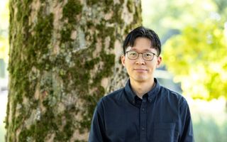 Portret van een Aziatische man met zwart haar, bril en donker overhemd.