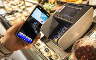 Iemand betaalt met zijn of haar telefoon bij een pinkassa in een supermarkt. Van de persoon zie je alleen de linkerhand.