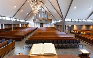 Interieur van een twintigste-eeuws kerkgebouw met bruine banken en een pijporgel achterin.