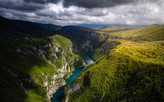 Bergen lijken bedekt met een groen tapijt. In het midden stroomt een blauwe rivier.