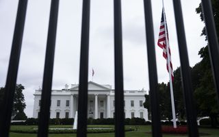 Groot wit gebouw met ervoor een hek waaraan een vlag halfstok hangt.