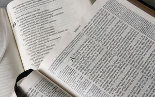 Tweetal Bijbels in verschillende vertalingen liggen bovenop elkaar, opengeslagen bij Jesaja 45.