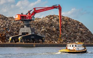 Een grote en hoge rode kraan op een rails naast het water van een kanaal waar een geel-wit bootje in vaart. 