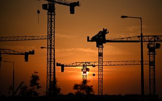 Hijskranen met op de achtergrond een ondergaande zon. 