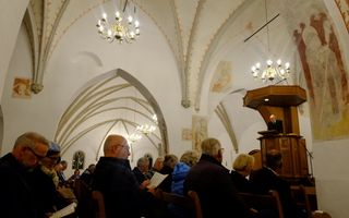 Mensen in de kerkbanken, op de preekstoel een man in zwart pak.