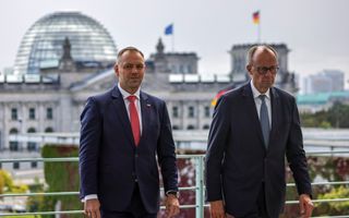 Twee mannen in pak staan op een dak. Op de achtergrond is een koepelvormig gebouw te zien 