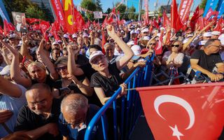Mensen steken hun armen in de lucht en zwaaien met rode vlaggen.