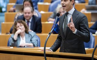 Man staat bij interruptiemicrofoon in de plenaire zaal van de Tweede Kamer. Achter hem zitten Kamerleden.