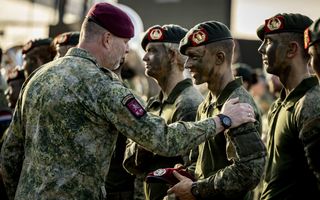 Officier legt hand op schouder van lachende jongen in camouflagekleding met geschminkt gezicht.