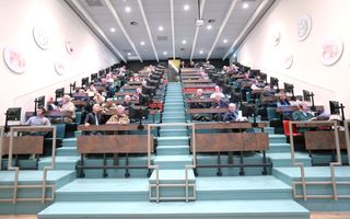 Veilinghal met kopers in bankjes. 