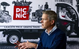 Man in blauwe trui voor een bezorgauto van Picnic. Daarop is een tas met booschappen afgebeeld.