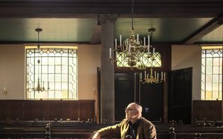 David Samama, een man met bril en zwart keppeltje op, zit op een bank in een oude synagoge.