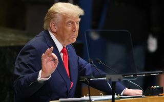 Een man in pak staat achter een katheder.