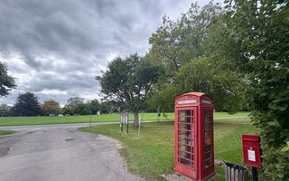 Een rode telefooncel staat op een grasveld in een park 