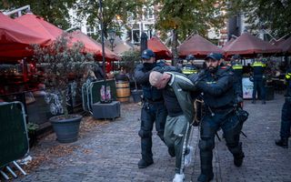 Twee politieagenten slepen een man in groen trainingspak het centrum van Den Haag uit. 