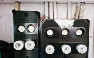 Zwarte kastjes met witte knoppen tonen een verouderde groepenkast voor de elektriciteitsvoorziening in de woning.