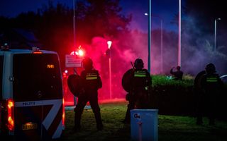 Drie met wapenstok en schild uitgeruste ME’ers staan tegenover in rook gehulde demonstranten.