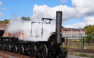 Een stoomtrein met ontzettend veel stoom; Engelstalig bord op de achtergrond. 