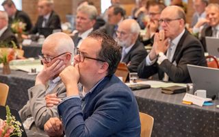 Mannen achter vergadertafels, in nadenkende houding.