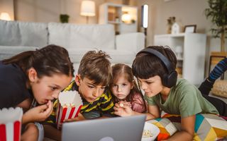 Vier popcorn etende kinderen kijken naar wat er op een laptop te zien is.