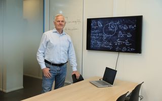 Man in spijkerbroek en overhemd bij een bord met wiskundige formules.