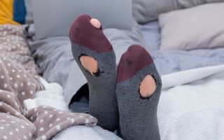 Blanke man zit op de bank met laptop in gescheurde sokken.