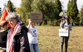 Mensen met spandoeken en vlaggen achter dranghekken.