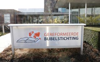 Gebouw met op de voorgrond wit bord met logo, Bijbel met wereldbol, van de Gereformeerde Bijbelstichting.
