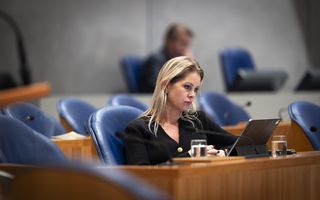 Vrouw zit in blauwe stoel in het kabinetsvak van de plenaire zaal van de Tweede Kamer met voor zich een tablet.