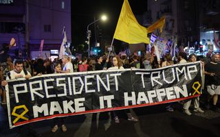 Mensen houden zwart spandoek met witte letters omhoog op straat.
