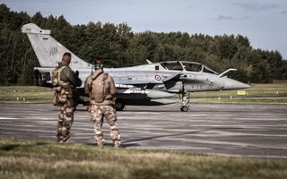 Twee soldaten in uniform staan bij een grijze straaljager 