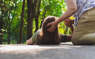 Een jonge vrouw ligt op straat. Een oudere vrouw houdt haar hoofd en hand vast. 