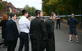 Jongemannen in donkeren pakken en keppeltjes op het hoofd staan op de weg bij politielint.
