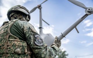 Een militair in camouflagekleding houdt in zijn handen een drone vast.